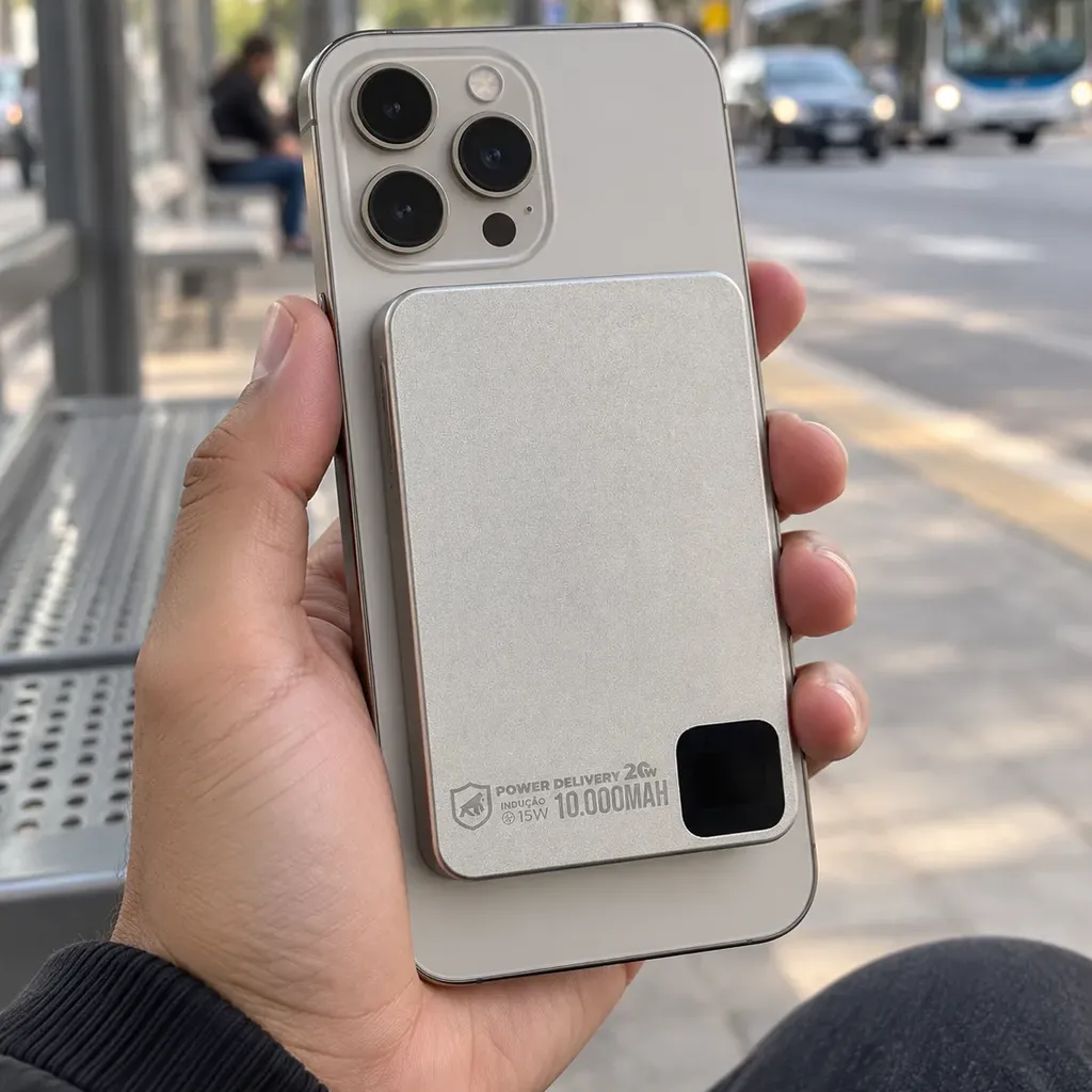 Mão segurando um celular com o carregador Gshield Titanium bege preso atrás pelo ímã, num ponto de ônibus